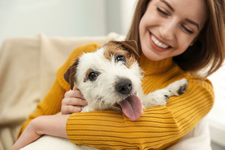 Woman in yellow sweater hugging a a white and brown dog.